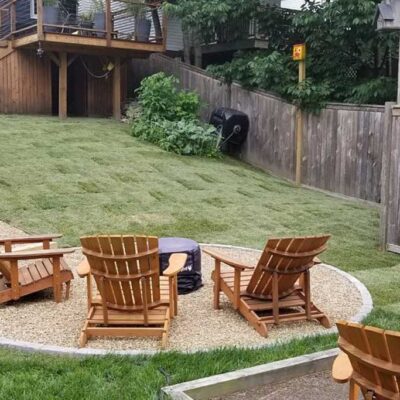 Custom hardscaped staircase leading down a sloping green lawn to a fire pit in a fenced yard.