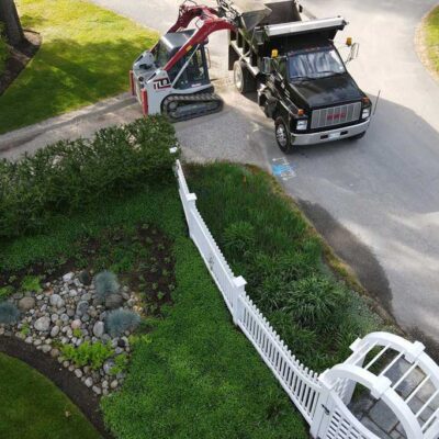 Trucks and hardscaping equipment in action at a residential work site with a gated garden.