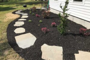 Flower garden on side of a residential home with flagstone path leading to the back patio.