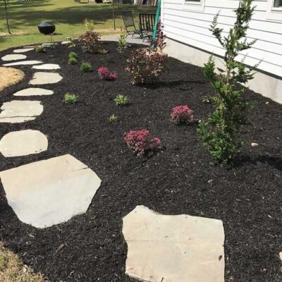 Flower garden on side of a residential home with flagstone path leading to the back patio.