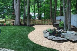 A custom backyard design by Willie C. & Sons Landscaping featuring a mulched path and rock-walled garden.