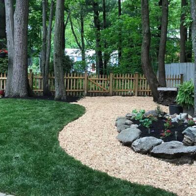 A custom backyard design by Willie C. & Sons Landscaping featuring a mulched path and rock-walled garden.