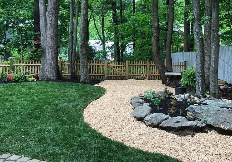 A custom backyard design by Willie C. & Sons Landscaping featuring a mulched path and rock-walled garden.